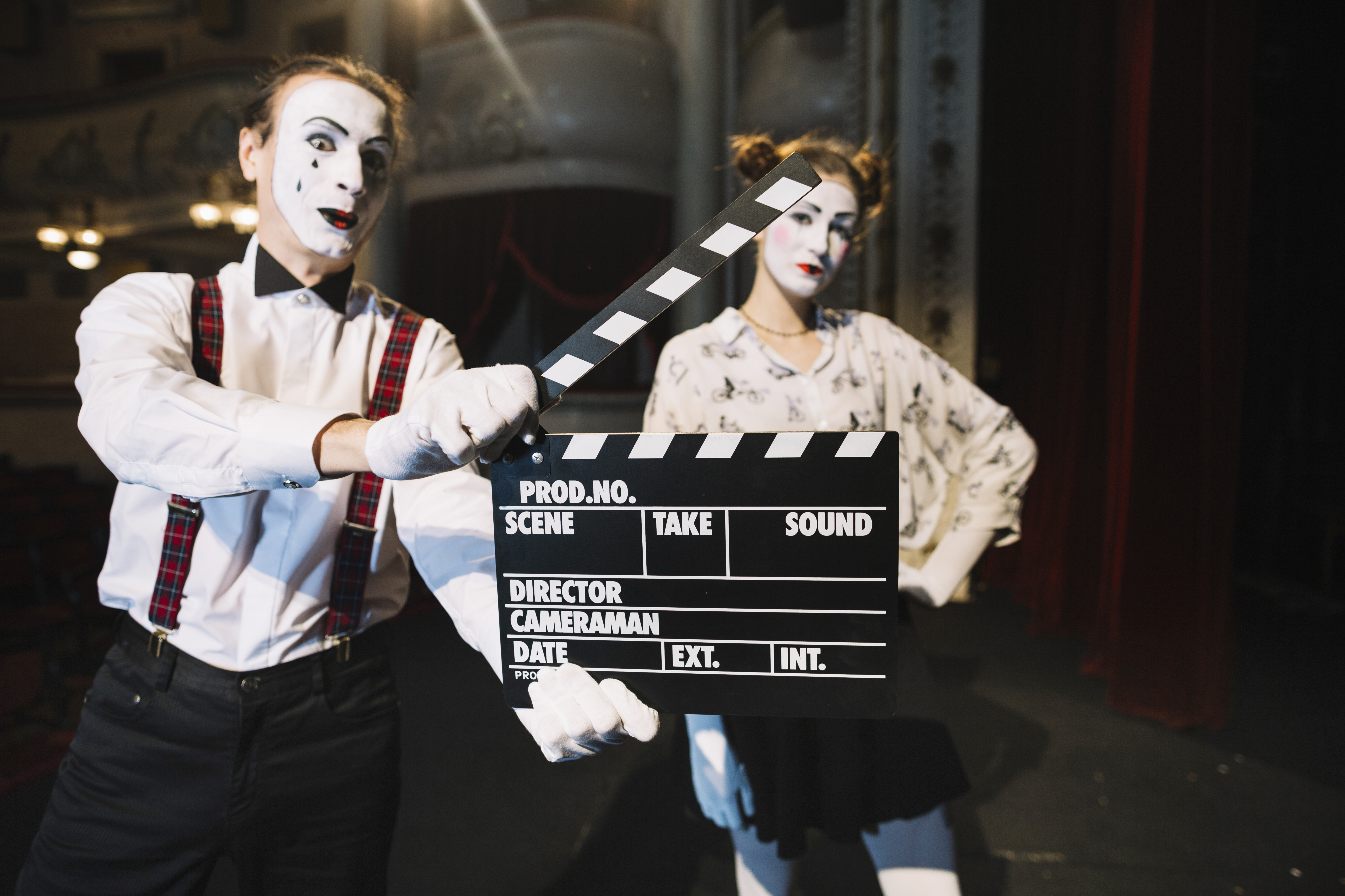 male mime artist holding clapper in front of female mime artist